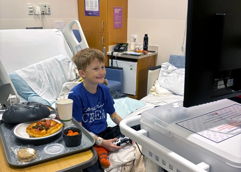 A boy happily plays video games on his GO Kart at the hospital with his pizza waiting.